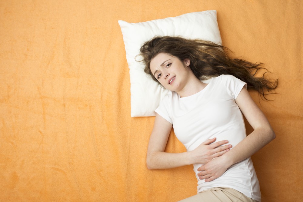 sick woman laying bed bed holding her stomach