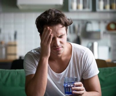 man holding a glass of water while rubbing his head from a hangover