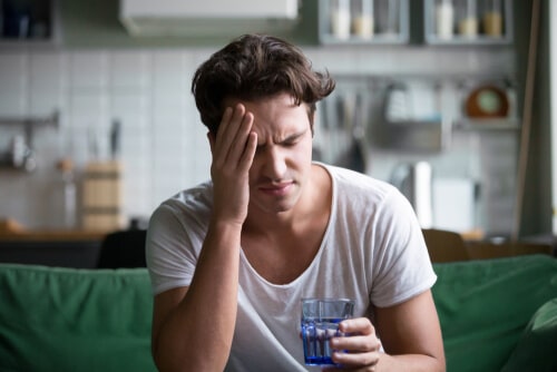 man holding a glass of water while rubbing his head from a hangover