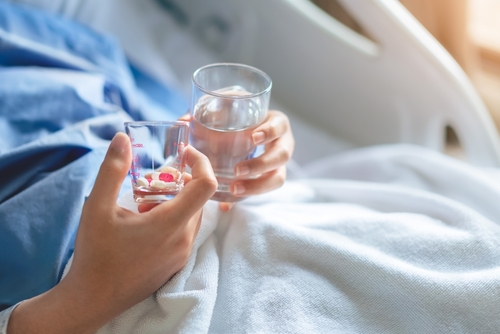 woman patient with medical drip or IV drip holding water with medicine in hospital